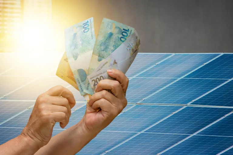 Fim da redução da tarifa de importação dos painéis montados incentivará a produção local de módulos fotovoltaicos 2 economia-de-energia-solar-segurando-dinheiro-brasileiro-em-frente-ao-painel-fotovoltaico-em-um-telhado-fundo-por-do-sol-espaco-para-texto